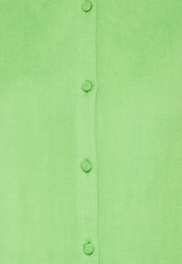 Camicia verde con bottoni, caratterizzata da una texture del tessuto, con sei bottoni sul davanti e cuciture a contrasto lungo i bordi.