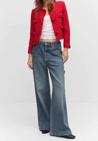 Blazer rouge texturé avec des boutons proéminents, associé à un jean à jambes larges bleu clair avec un effet délavé et des poches latérales. Talons noirs.