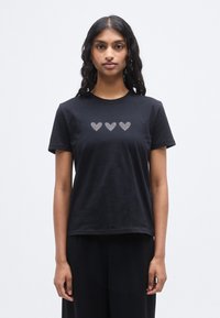 Μαύρο βαμβακερό t-shirt με στρογγυλή λαιμόκοψη και κοντά μανίκια, διακοσμημένο με τρεις καρδιές από μικρά στρας στο μπροστινό μέρος.