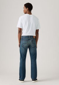 Dark blue denim jeans with a straight cut, visible stitching, and two back pockets. Paired with a plain white t-shirt.