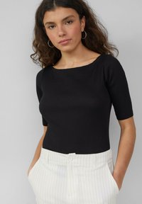 Czarny żeberkowany top z krótkim rękawem i szerokim dekoltem, zestawiony z białymi spodniami w prążki. Tkanina ma teksturowane wykończenie.