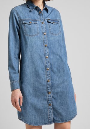 Vestido camisero de mezclilla en azul claro con mangas largas, botones en la parte delantera, dos bolsillos en el pecho y dobladillo curvo. Cuenta con botones de tono dorado.