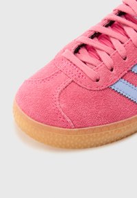 Rosa semskesneaker med en teksturert overflate, med rosa lisser og lyseblå striper, komplementert av en såle av gummi.
