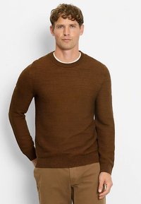 Brauner Pullover mit Struktur, Rundhalsausschnitt, langen Ärmeln und geripptem Saum. Kombiniert mit beigen Hosen vor weißem Hintergrund.