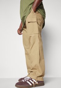 Beige cargo broek met zijzakken, van katoen, losse pasvorm en een omgeslagen zoom, gecombineerd met donkerpaarse sneakers met witte strepen.