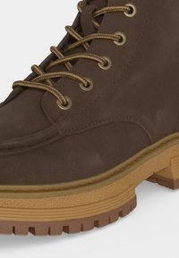Botte de randonnée en daim marron avec des lacets marron et beige à motifs, des œillets en laiton et une semelle épaisse en caoutchouc texturé avec une profonde semelle.