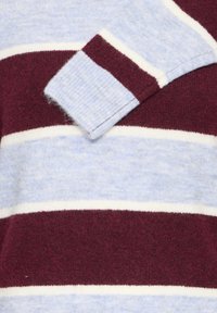 Manche et corps de pull en maille douce avec de larges rayures horizontales en bordeaux et bleu clair séparées par de fines lignes blanches.