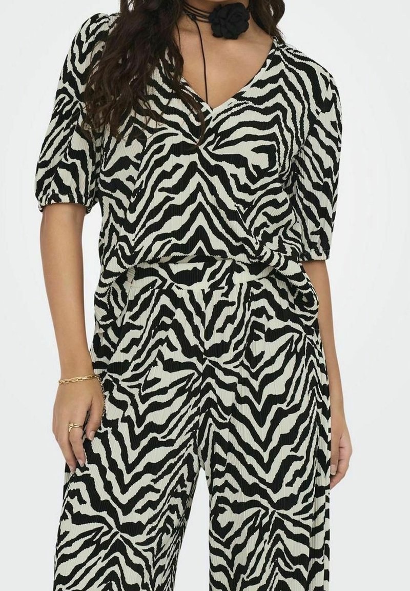 Černobílý top s zebrovaným vzorem, krátkým rukávem a výstřihem do V, spárovaný s odpovídajícími kalhotami. Materiál má jemně ribbovanou strukturu.