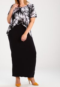 Robe longue noire avec un haut fluide à motif floral noir et blanc. La tenue présente une coupe décontractée et est associée à des escarpins jaunes à bout pointu.