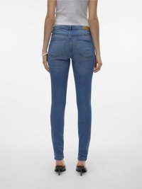 Modré denimové skinny jeans s hladkou textúrou, stredným pásom a dvoma zadnými vreckami, v kombinácii s čiernymi vysokými podpätkami.