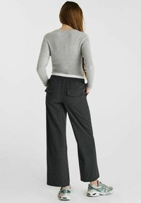 Haut à manches longues gris à rayures associé à un pantalon large à rayures noires avec taille élastique et deux poches arrière.