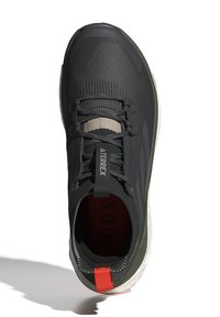 Chaussure de sport noire avec une tige en tissu texturé, accents gris, lacets élastiques et une languette rouge à l'arrière. La semelle intermédiaire présente une bande blanche.