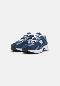Zapatillas deportivas azules con materiales de malla y ante, detalles en blanco y cordones. Suela acolchada y diseño de punta redondeada.