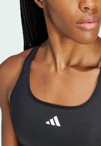 Svart treningstopp med avrundet halslinning, med hvit logo-detalj på venstre side, glatt stoff og racerback-design.