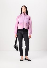 Fleece striukė su gradientine rožine spalva, užtrauktuko uždarymas, dvi priekinės kišenės, elastinės rankovės, derinama su juodu marškinėliu ir džinsais, bei maža juoda rankine.