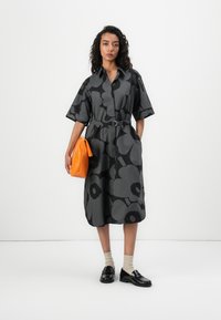 Flowing black dress with large gray floral pattern, belted at the waist. Paired with an orange handbag and black loafers. Neutral socks.