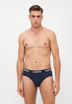 Marineblaue Levi's Slips mit einem kontrastierenden Logo-Bund. Glattes Material mit schmalem Schnitt. Modell steht, oberkörperfrei und auf neutralem Hintergrund.