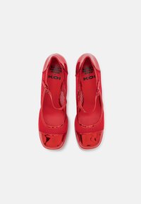Zapatos rojos con puntera de charol, paneles laterales de malla y correa ajustable. Textura suave con un acabado brillante.
