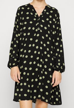 Vestido negro con mangas largas, escote en V, lunares verdes y detalles de botones. La tela parece suave y ligera, con una forma acampanada.