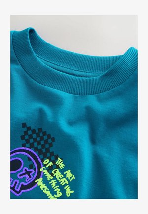 Türkisfarbenes Baumwoll-T-Shirt mit einem gerippten Rundhalsausschnitt, mit grafischen Aufdrucken in Lila und Schwarz sowie einem Schachbrettmuster im Design.