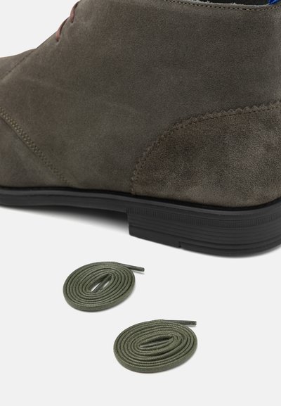 Pruun sametist sokk, millel on must kummitald. Kaks roheline paela on läheduses keritud, millel on tekstureeritud pind ja teravad otsad.