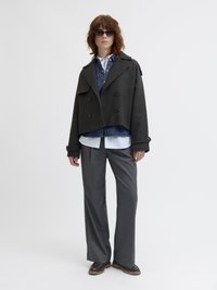 Skrajšani črni plašč s karo vzorcem in dvorednim zapiranjem, oblečen čez jeansahem srajco in belo črtasto srajco, v kombinaciji z sivo širokima hlačami.