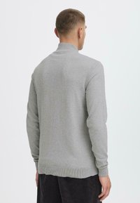 Maglione grigio lavorato a maglia con colletto alto, maniche lunghe e orlo a costine. La texture appare morbida e liscia, progettata per il comfort.