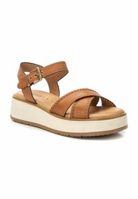 Sandal de piel marrón con tiras entrelazadas, cierre de hebilla y suela de plataforma blanca. Cuenta con detalles de costura en las tiras.