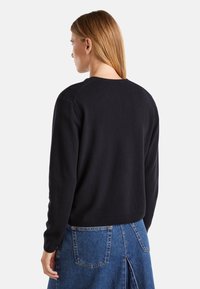 Černý vlněný svetr s kulatým výstřihem a dlouhými rukávy, s texturovaným povrchem; kombinovaný s modrou džínovou sukní.