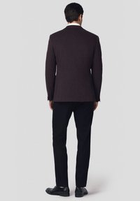 Ciemnofioletowy żakiet na miarę, z jednym rozcięciem, noszony na czarnych spodniach. Gładki design z gładkiego materiału i minimalistycznymi akcentami. Czarne buty.