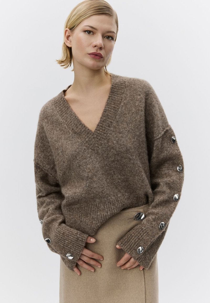 Pulover maro din amestec de lână, cu decolteu în V, croială oversized și accente de nasturi argintii pe mâneci. Textură moale și tiv cu rebei.