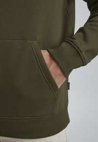 Sudadera verde oliva con bolsillo tipo canguro, puños acanalados y una textura suave. El dobladillo cuenta con una costura reforzada para mayor durabilidad.