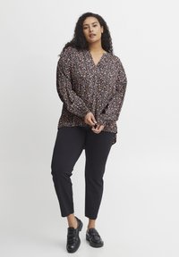 Melna ziedu blūze ar garām piedurknēm un V veida izgriezumu, kas rotāta ar krāsainiem rakstiem. Blūze ir brīva piegriezumā un apvienota ar melniem šauros biksēm un melniem apaviem.