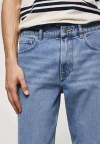 Jeans in denim azzurro chiaro con taglio classico, dotati di cinque tasche e chiusura a bottone. Il tessuto presenta una superficie leggermente strutturata.