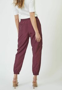 Bordo tapered trenirke s elastičnim strukom i manžetama, izrađene od glatkog, laganog materijala. Uparene s prozirnim štiklama.