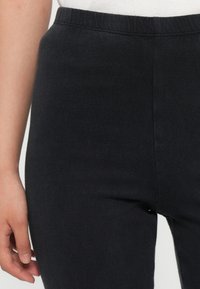 Leggings pretos com cintura elástica, confeccionados em um tecido liso e elástico. Design ajustado sem costuras ou padrões visíveis.
