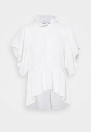 Blusa blanca con cuello alto con volantes, mangas campana y dobladillo asimétrico con peplum, presentada sobre un fondo claro y liso.