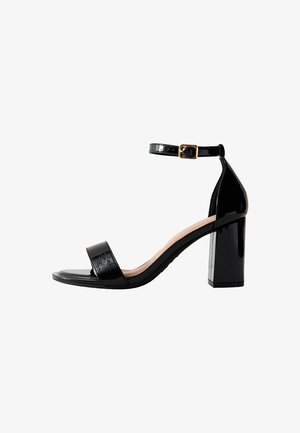 Zwarte gepatineerde leren sandalen met blokhak, voorzien van een brede enkelband met gesp, met een gladde textuur en minimalistisch design.