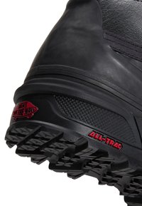 Κοντινή λήψη της μαύρης σόλας μιας μπότες Vans με βαθιά πέλματα και κόκκινα λογότυπα "Vans Off The Wall" και "All-Trac" στη φτέρνα.