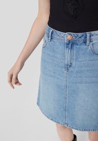 Jasnoniebieska spódnica w kształcie litery A z dżinsu, z przednim zapięciem na guziki, kontrastującymi przeszyciami oraz lekko zakrzywionym dołem. Gładka tekstura i swobodny design.