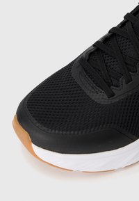 Black athletic shoe with a mesh upper, textured black overlays, black laces, and a white midsole. Features a brown rubber outsole.
