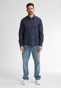 Merihenkinen napitettava paita, jossa on normaali kaulus ja pitkät hihat, yhdistettynä vaaleansinisiin farkkuihin ja valkoisiin tennareihin. Yksinkertainen, rento muotoilu.