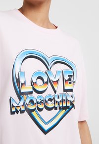 Růžové bavlněné tričko s velkým grafickým potiskem, který zobrazuje text "LOVE MOSCHINO" v designu barevného srdce, kulatý výstřih, krátké rukávy.