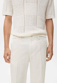 White knitted short-sleeve sweater with open weave pattern, paired with light beige linen trousers featuring a straight cut and front pleats.