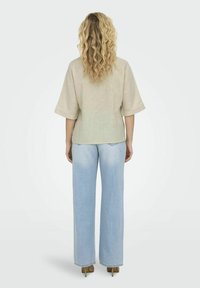 Beige linnedragt med brede ærmer, parret med lyseblå højtaljede flared jeans. Bemærk det teksturerede stof og det afslappede design.