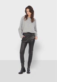 Šedý svetr s dlouhými rukávy, v kombinaci s černými koženými jogger kalhotami, které mají elastický pás a přední kapsy. Černé kotníkové boty.