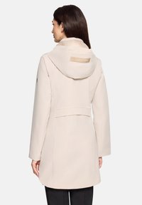 Beżowy wodoodporny płaszcz z kapturem, z tylną karczkiem, bocznymi kieszeniami oraz subtelną fakturą tkaniny; na kapturze wytłoczona etykieta "CROSSOVER".