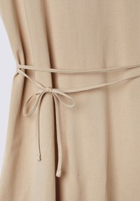 Abito di stoffa beige con una texture morbida, caratterizzato da un dettaglio in vita legato e un design fluido e morbido.