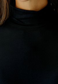Schwarzes Rollkragenoberteil aus weichem Stoff, mit einem figurbetonten Design und glatter Textur, sowie einem hohen Kragen, der den Hals bedeckt.