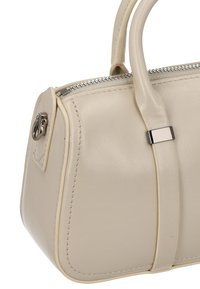 Beige Lederhandtasche mit einer strukturierten Form, versehen mit einem silbernen Reißverschluss, Nahtdetails und einem dekorativen Riemen.